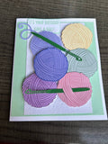 Handmade birthday card with six layered pastel paper yarn balls and two green crochet hooks on a mint and white background, reading It’s your birthday, have a ball