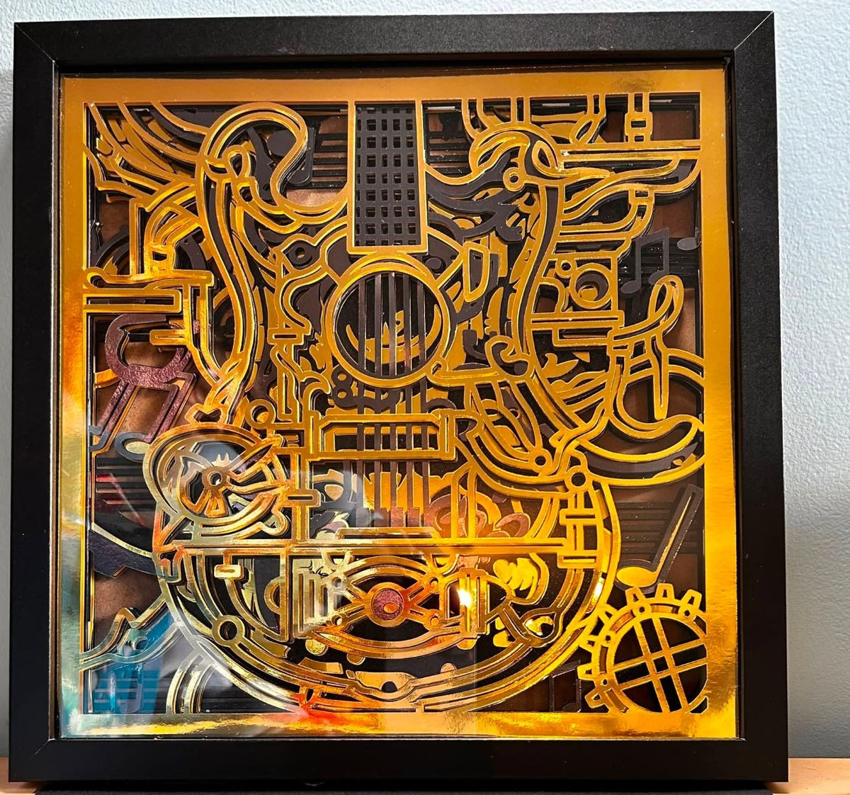 Handmade layered shadow box with a guitar, music notes, and gears in mirror-gold and dark paper layers in a black frame
