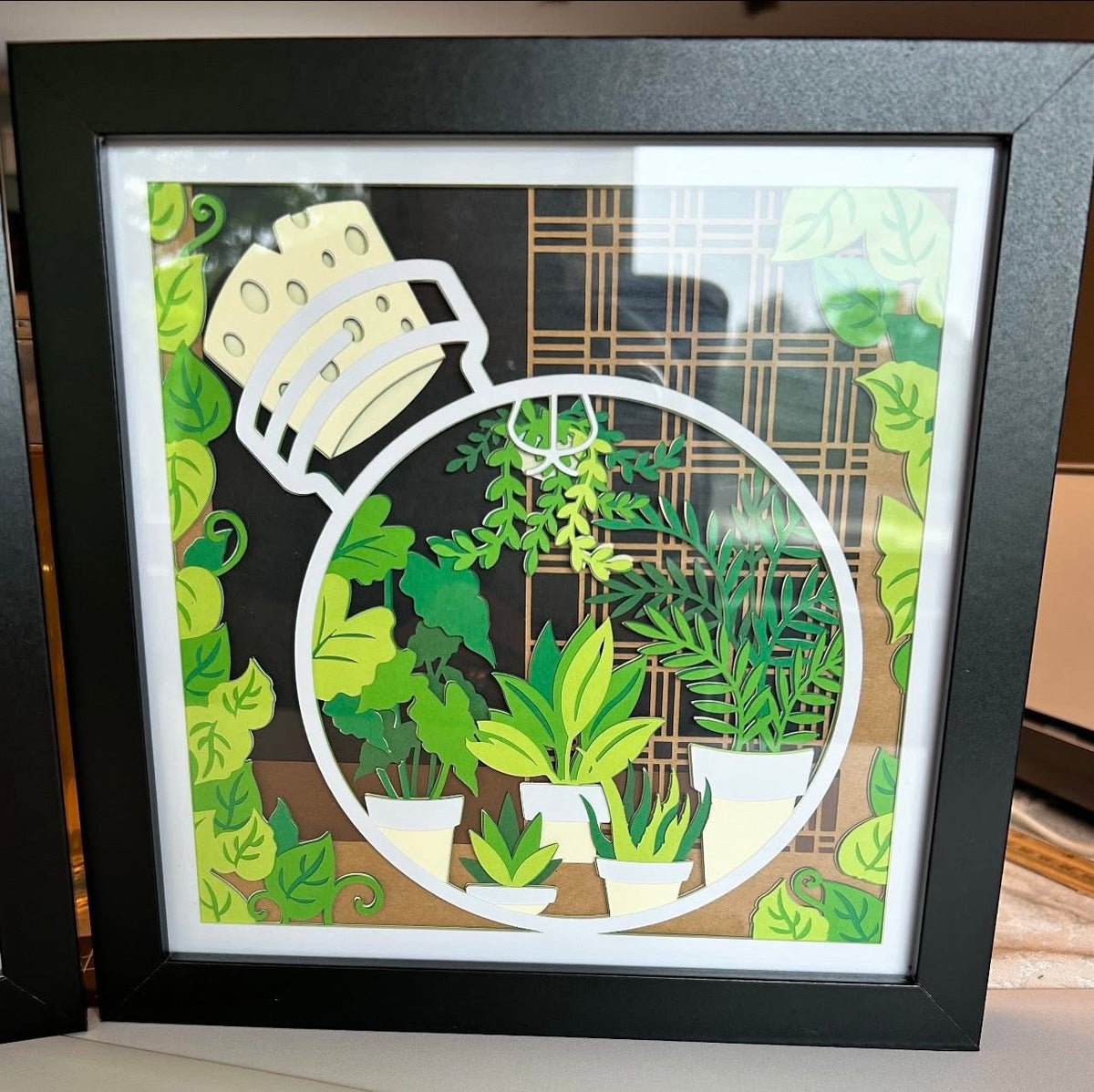 Handmade plant terrarium layered paper shadow box with potted plants and vines in a black frame